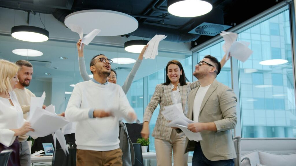 Diverse team celebrating by throwing papers in office